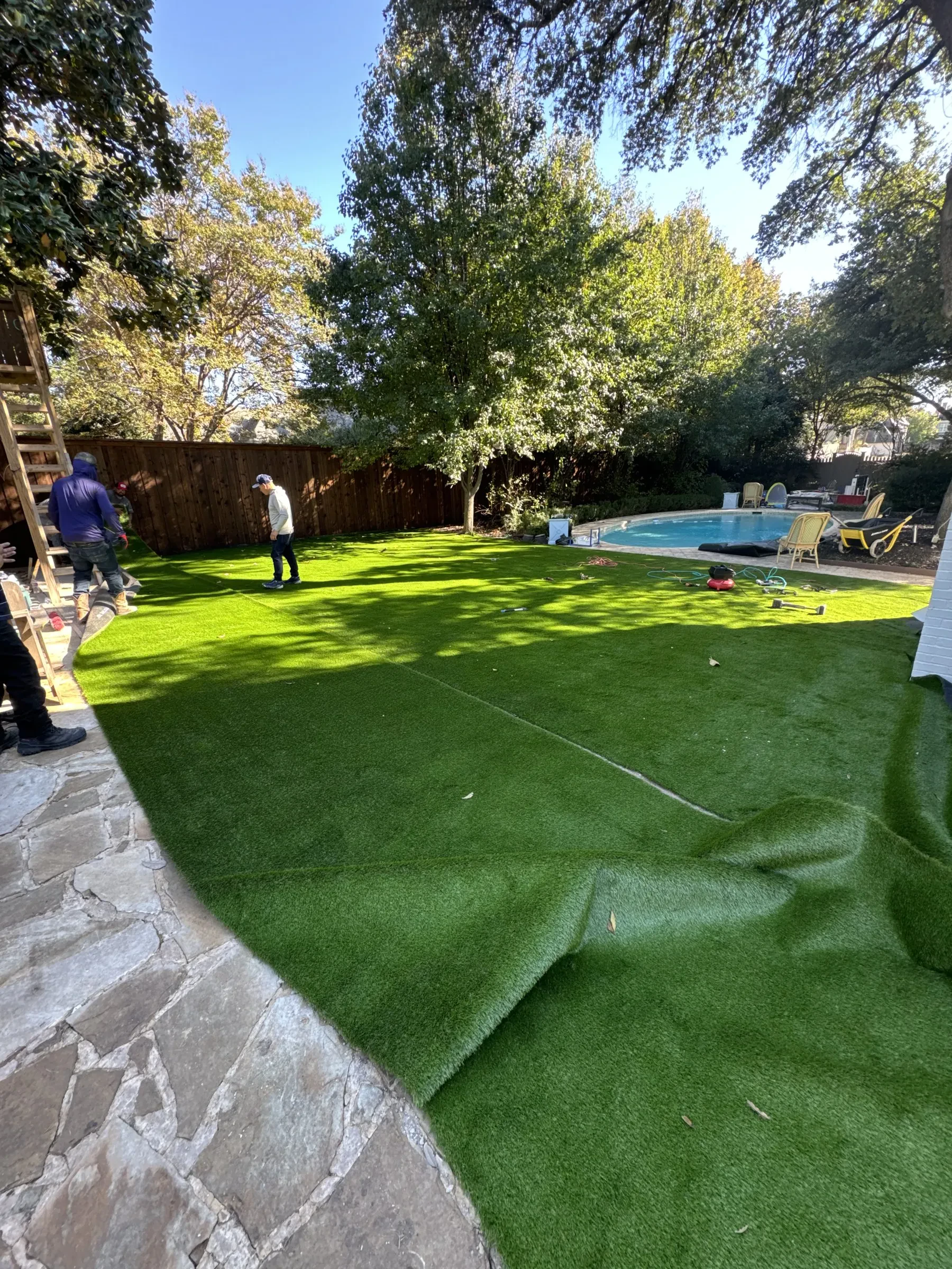 Artificial turf rolls being fitted beside a pool